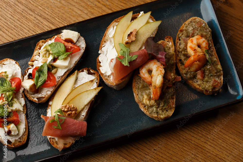 Bruschettas with vegetables. Start dishes with cherry tomatoes, avocado, cream cheese and shrimps. Food composition, tasty italian meal