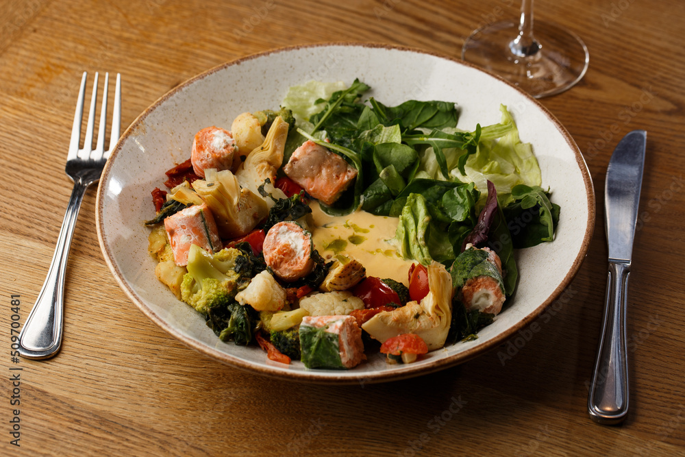 A salad with grilled salmon, mashed avocado and lettuce dressed with cream cheese. Close-up of the dish in a brown bowl isolated on brown background.