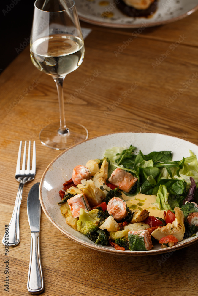A salad with grilled salmon, mashed avocado and lettuce dressed with cream cheese. Close-up of the dish in a brown bowl isolated on brown background.