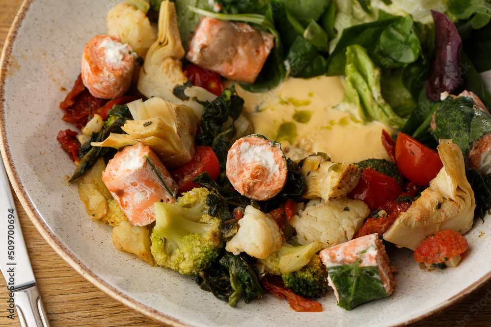 A salad with grilled salmon, mashed avocado and lettuce dressed with cream cheese. Close-up of the dish in a brown bowl isolated on brown background.