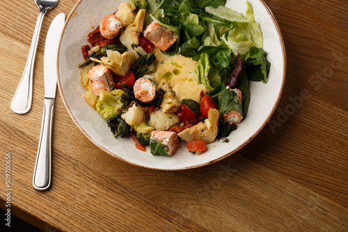 Obraz na płótnie A salad with grilled salmon, mashed avocado and lettuce dressed with cream cheese. Close-up of the dish in a brown bowl isolated on brown background. w salonie