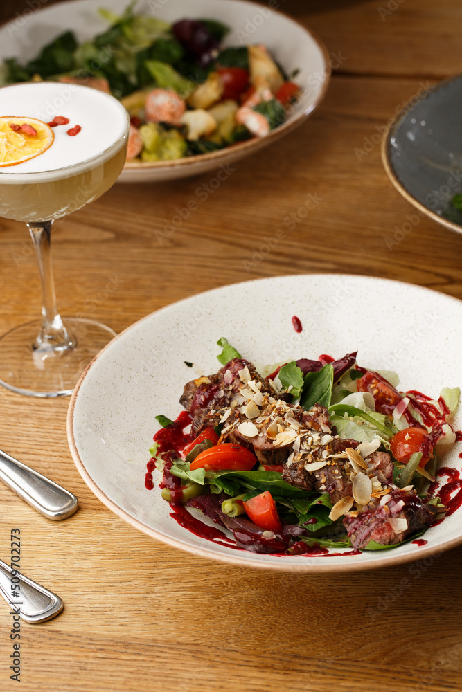 Salad with veal and tomatoes. Beef steak with raw vegetables mix side view. Grilled meat with garnish close-up. Delicious main course on table