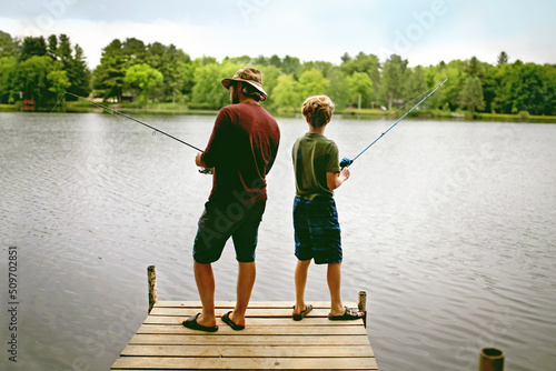 A happy father and his young son are fishing on a dock on a lake on a summer vacation.