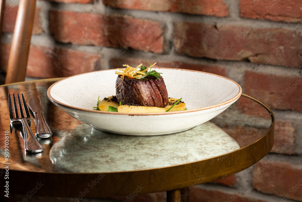 Grilled meat fillet steak medallion with green sauce, served with pear or apple. On dark background