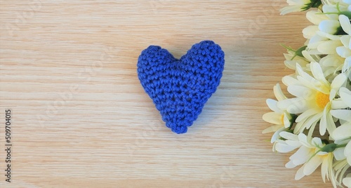 Flowers and a crochet heart on wooden background.