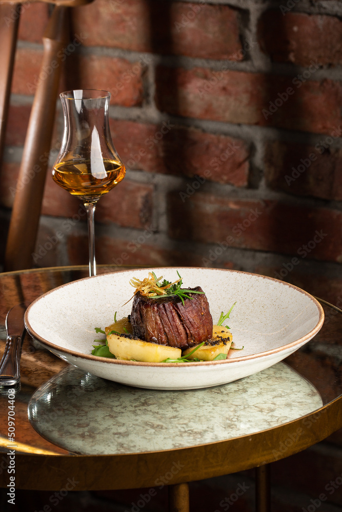 Grilled meat fillet steak medallion with green sauce, served with pear or apple. On dark background