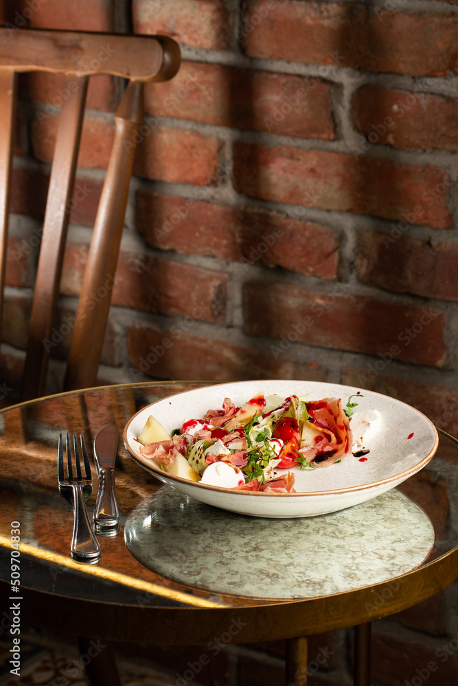 Prosciutto crudo ham salad with mozzarella cheese and arugula on a plate. Bright background. Top view. Copy space