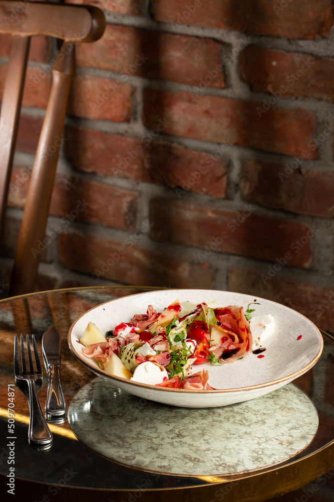 Prosciutto crudo ham salad with mozzarella cheese and arugula on a plate. Bright background. Top view. Copy space