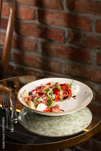 Prosciutto crudo ham salad with mozzarella cheese and arugula on a plate. Bright background. Top view. Copy space