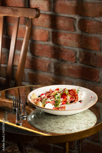 Obraz na płótnie Prosciutto crudo ham salad with mozzarella cheese and arugula on a plate. Bright background. Top view. Copy space w salonie