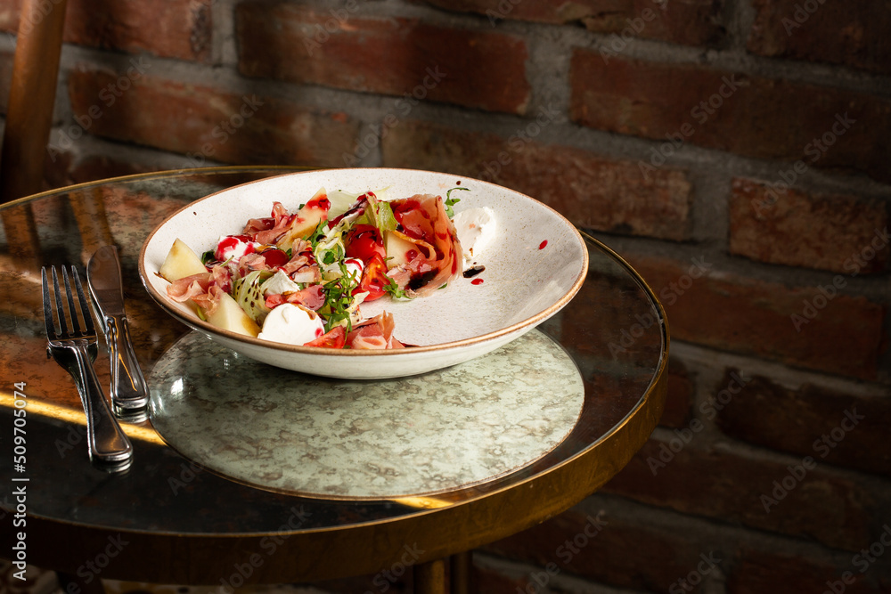 Prosciutto crudo ham salad with mozzarella cheese and arugula on a plate. Bright background. Top view. Copy space