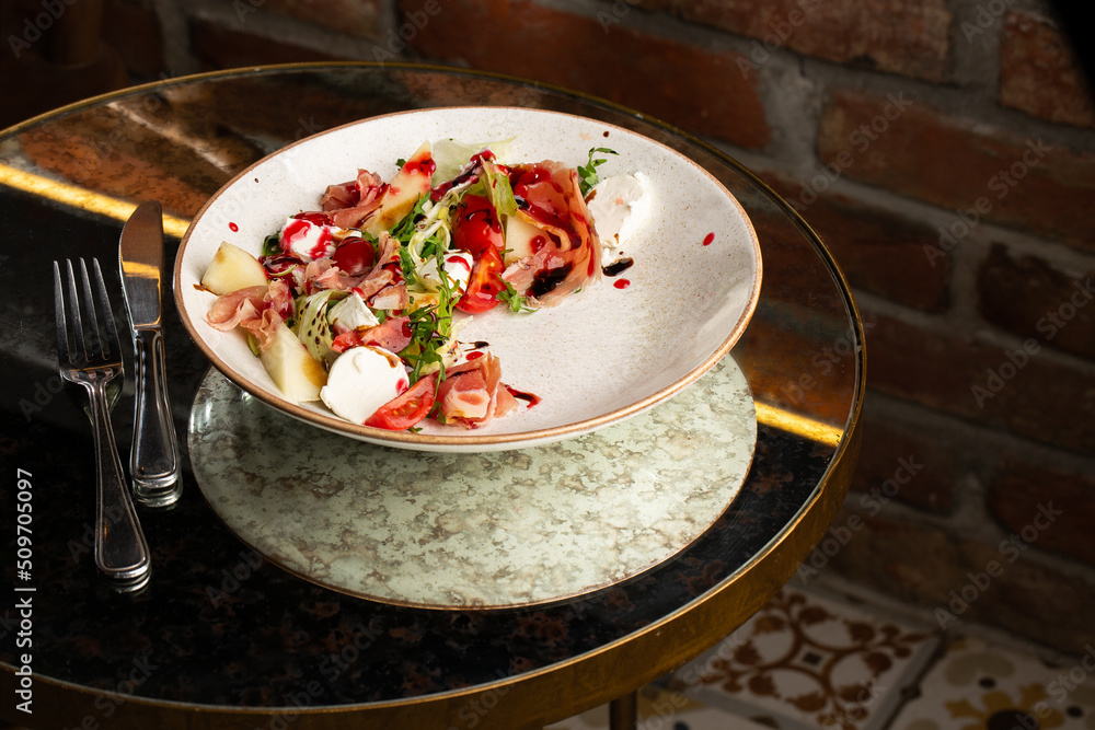 Prosciutto crudo ham salad with mozzarella cheese and arugula on a plate. Bright background. Top view. Copy space