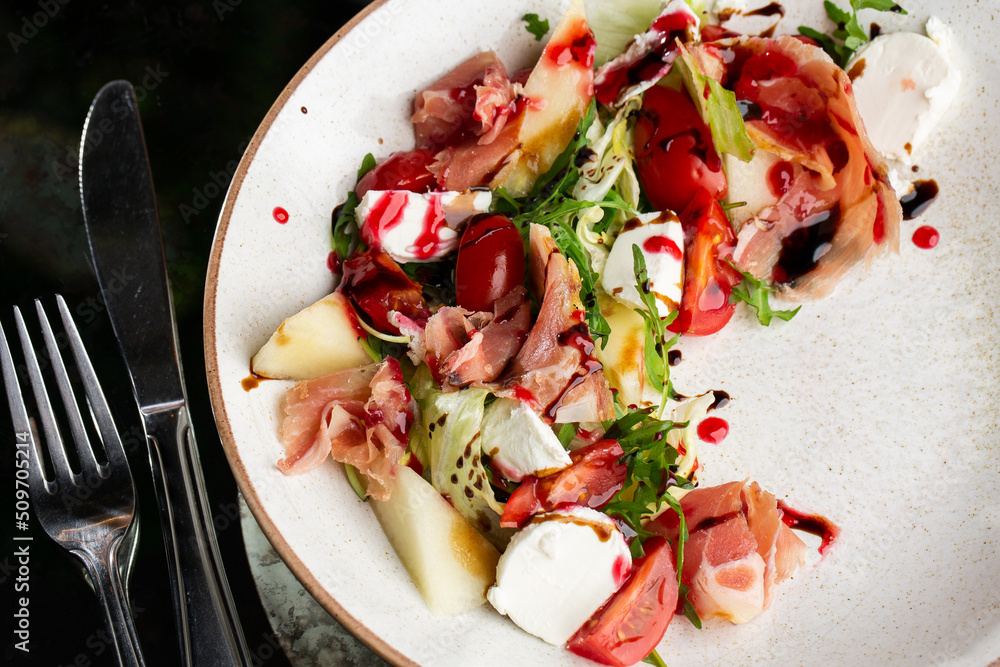 Prosciutto crudo ham salad with mozzarella cheese and arugula on a plate. Bright background. Top view. Copy space