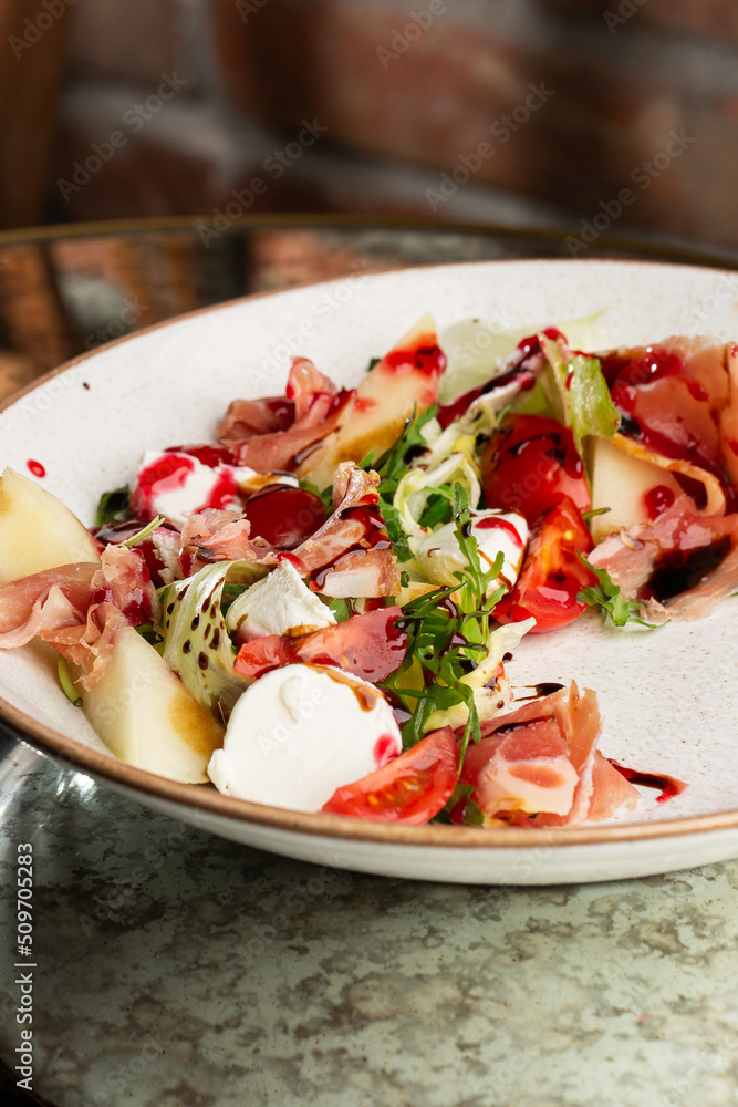 Prosciutto crudo ham salad with mozzarella cheese and arugula on a plate. Bright background. Top view. Copy space