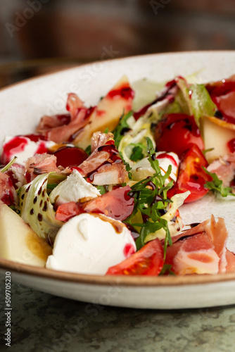 Prosciutto crudo ham salad with mozzarella cheese and arugula on a plate. Bright background. Top view. Copy space