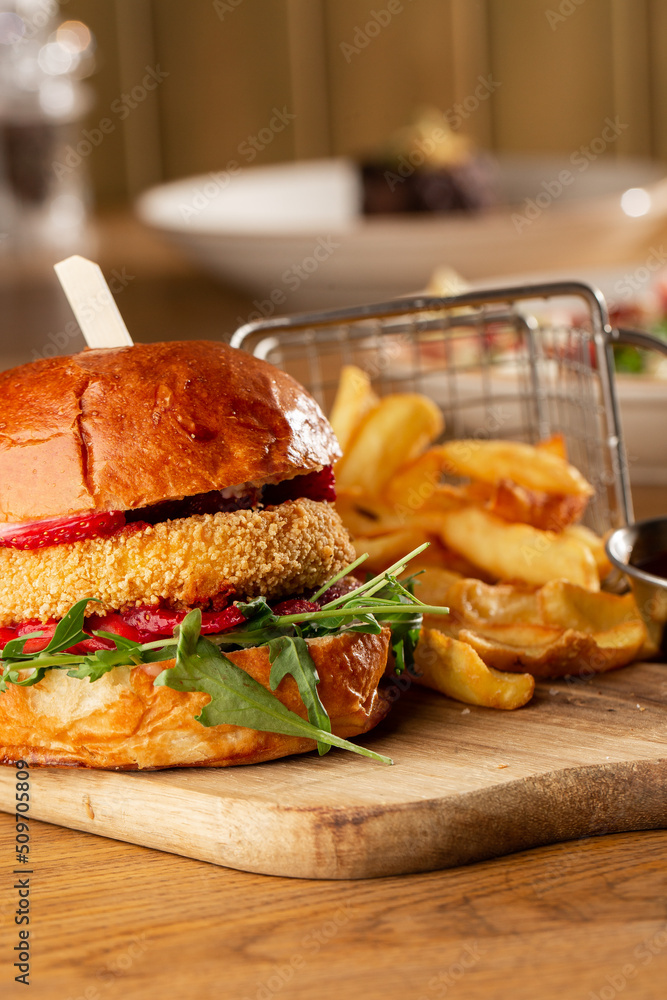 Big cheeseburger with french fries. Hamburger with beef patty onion, tomato, lettuce pickles, melted cheddar, mustards, tomato jam, mayo