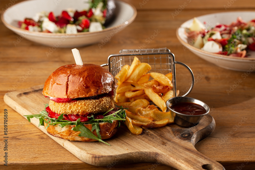 Big cheeseburger with french fries. Hamburger with beef patty onion, tomato, lettuce pickles, melted cheddar, mustards, tomato jam, mayo