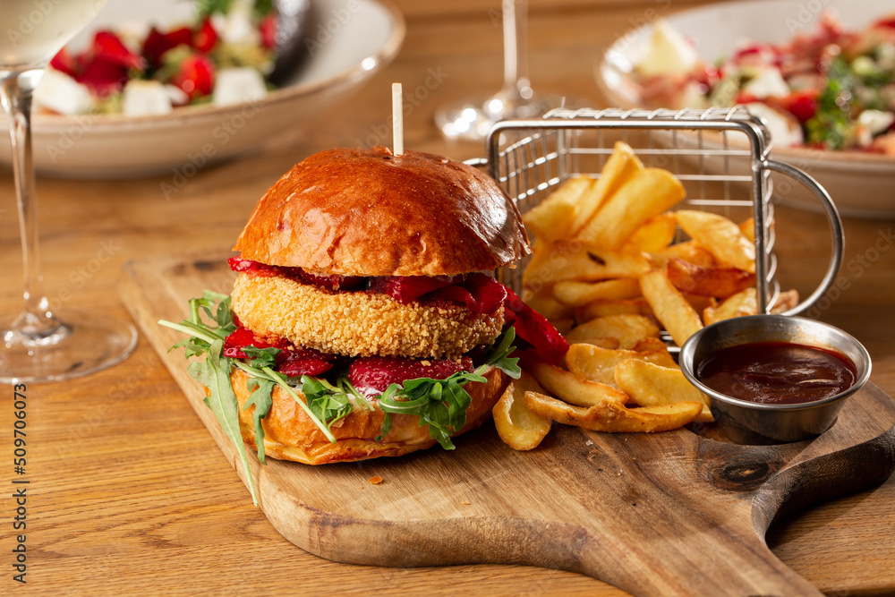 Big cheeseburger with french fries. Hamburger with beef patty onion, tomato, lettuce pickles, melted cheddar, mustards, tomato jam, mayo