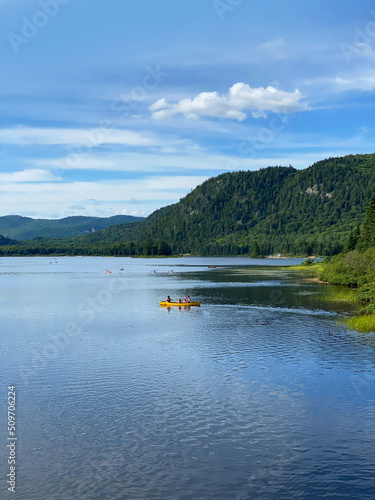 Paysage en été d'un lac entouré de montagnes. Gens au loin qui font du canot et du kayak sur la rivière.