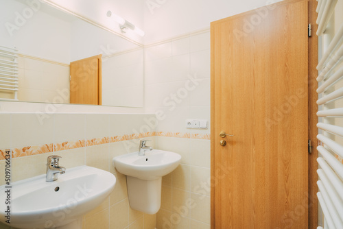 Small ordinary bathroom with retro tiles in an older hotel room. Everything is beautifully clean. The bathroom has common equipment such as whasbasins, mirrors, lamps and so on. The doors are wooden.