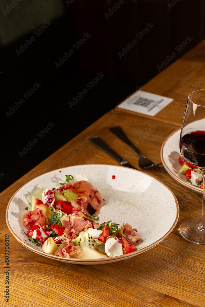 Prosciutto crudo ham salad with mozzarella cheese and arugula on a plate. Bright background. Top view. Copy space