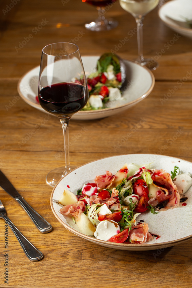 Prosciutto crudo ham salad with mozzarella cheese and arugula on a plate. Bright background. Top view. Copy space