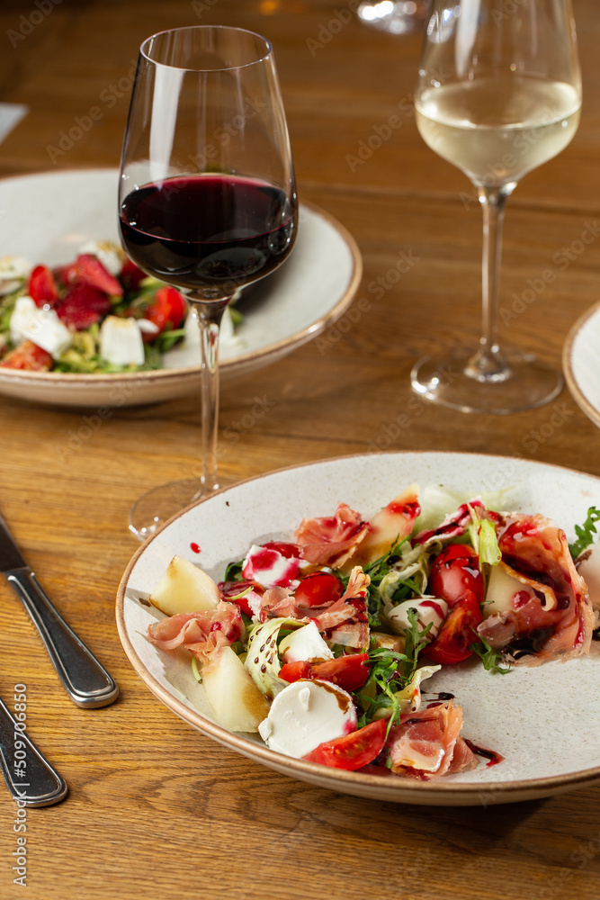 Prosciutto crudo ham salad with mozzarella cheese and arugula on a plate. Bright background. Top view. Copy space