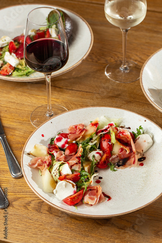 Prosciutto crudo ham salad with mozzarella cheese and arugula on a plate. Bright background. Top view. Copy space