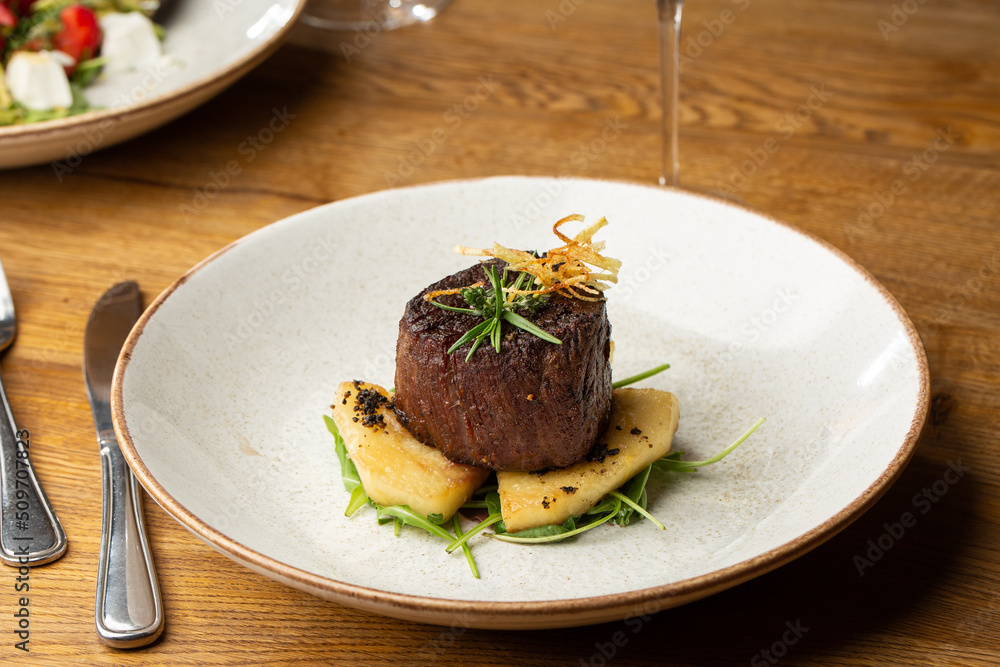 Grilled meat fillet steak medallion with green sauce, served with pear or apple. On dark background