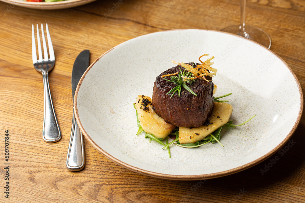 Grilled meat fillet steak medallion with green sauce, served with pear or apple. On dark background