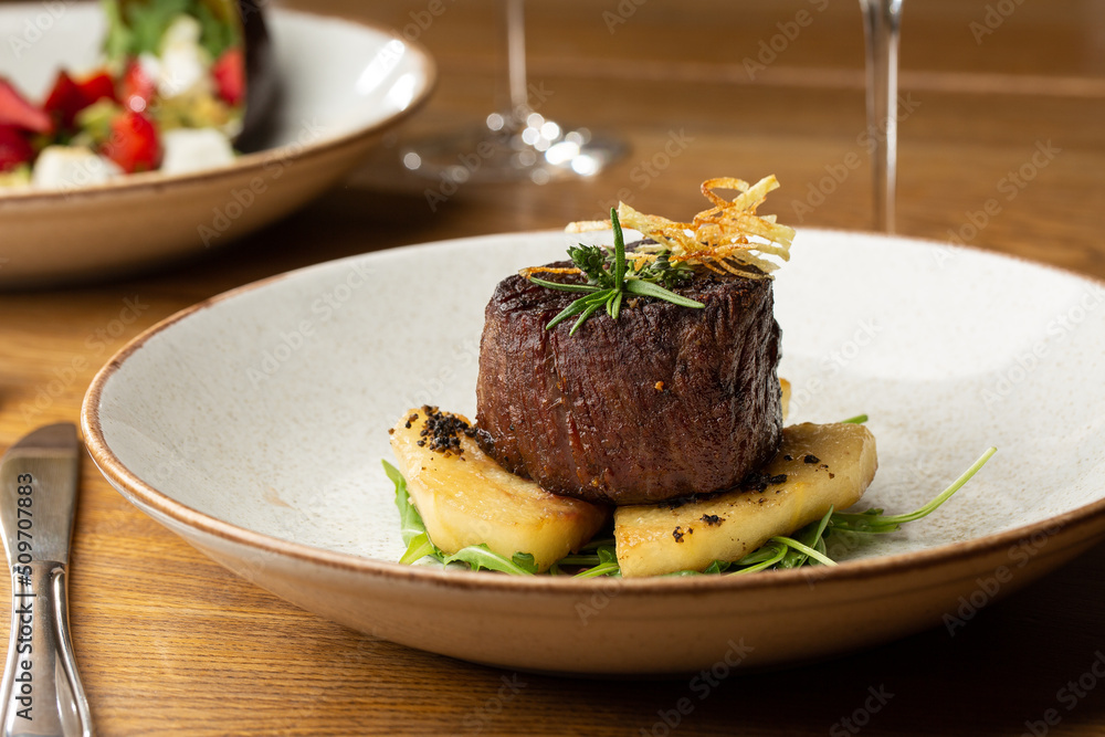 Grilled meat fillet steak medallion with green sauce, served with pear or apple. On dark background