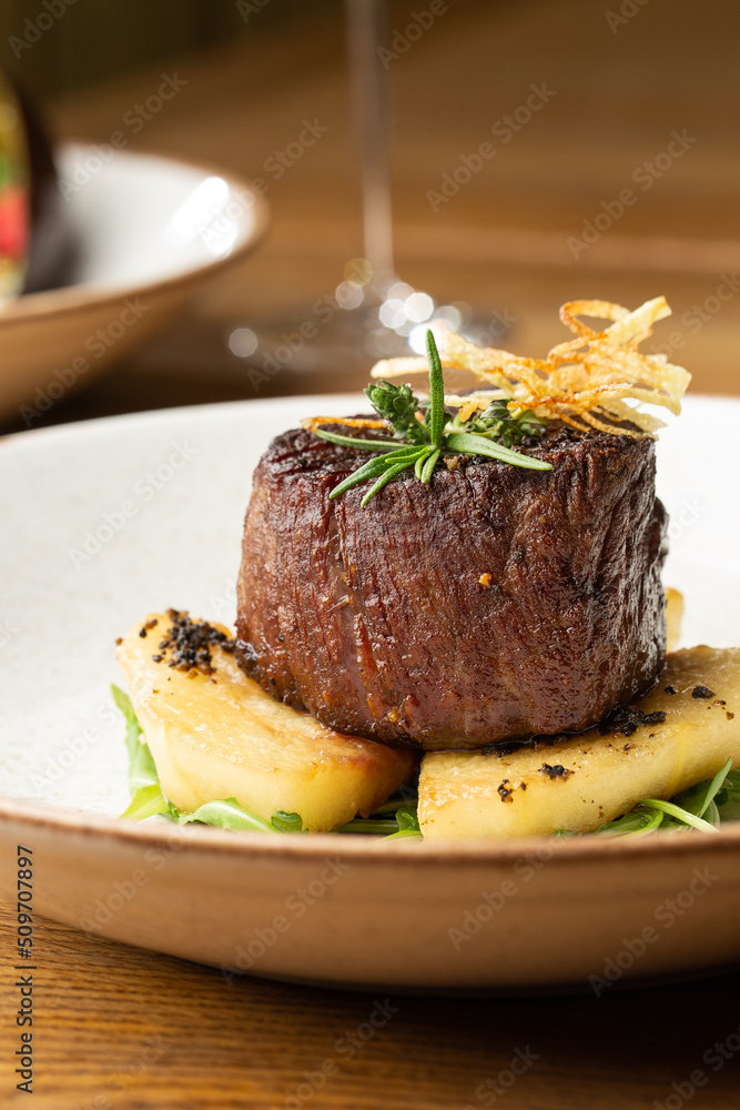 Grilled meat fillet steak medallion with green sauce, served with pear or apple. On dark background