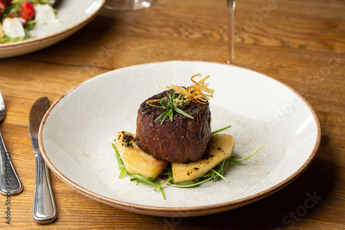 Grilled meat fillet steak medallion with green sauce, served with pear or apple. On dark background