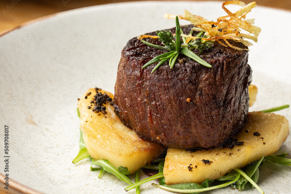Grilled meat fillet steak medallion with green sauce, served with pear or apple. On dark background