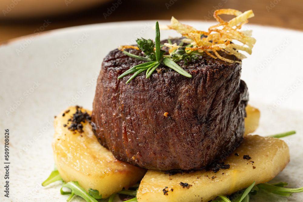 Grilled meat fillet steak medallion with green sauce, served with pear or apple. On dark background
