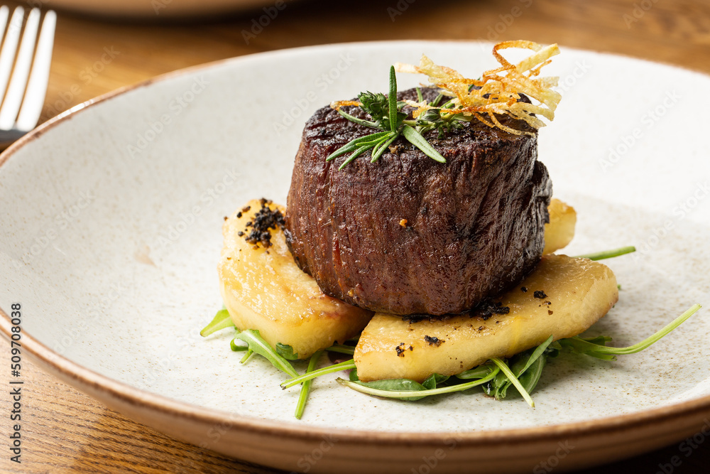 Grilled meat fillet steak medallion with green sauce, served with pear or apple. On dark background