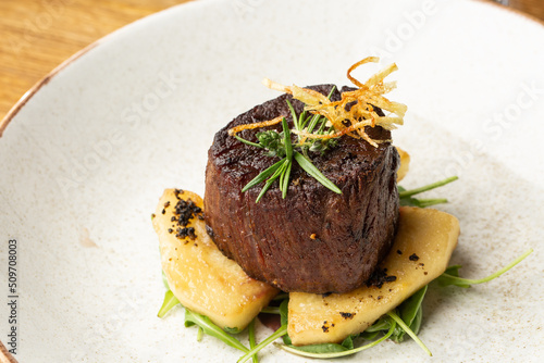 Grilled meat fillet steak medallion with green sauce, served with pear or apple. On dark background