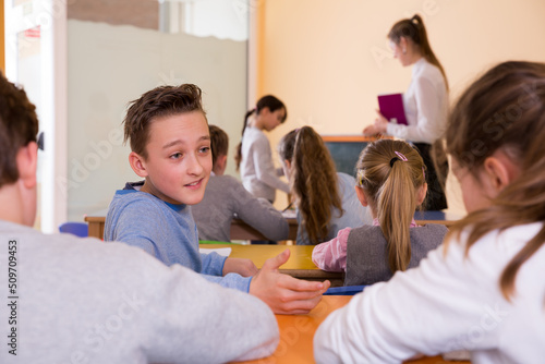 Fotografija Happy pupils chattering sitting on back desks at lesson in elementary school