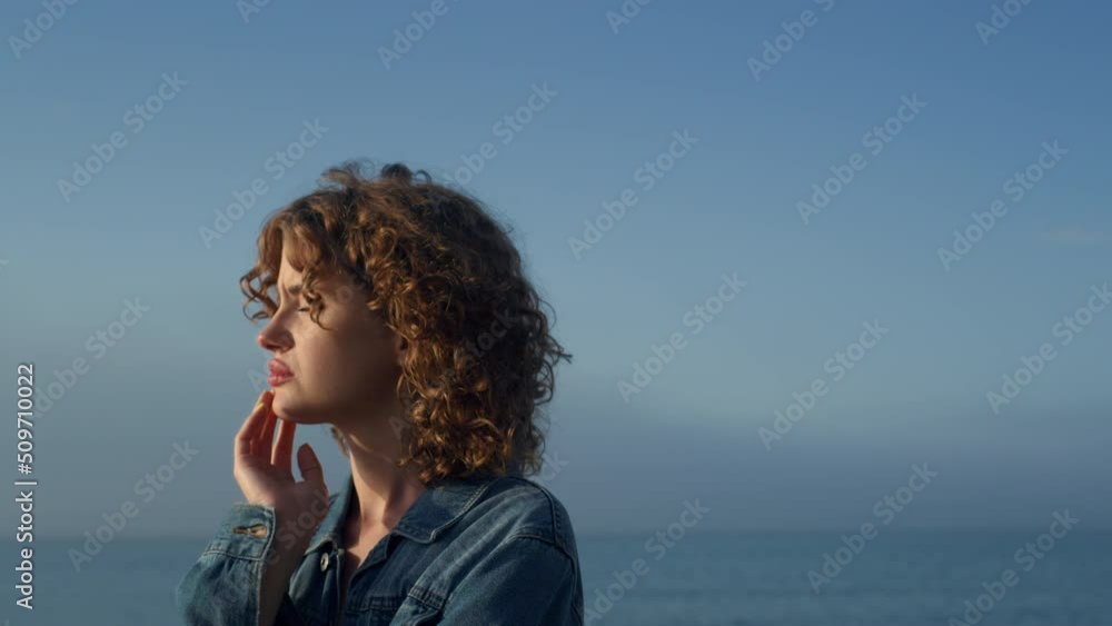 Sad woman standing on sea beach. Portrait of upset girl holding hand on face Sad woman standing on sea beach. Portrait of upset girl holding hand on face