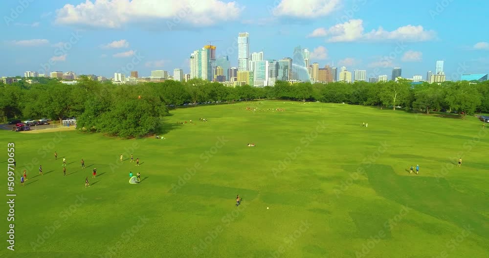 People playing sports in Zikler Park in Austin, Texas with the city skyscrapers in the background. Drone footage flying towards the city. People playing sports in Zikler Park in Austin, Texas with the city skyscrapers in the background. Drone footage flying towards the city.