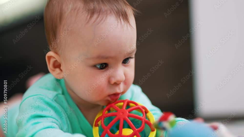 Baby boy lies on belly with his face to the camera. Close up. Adorable kid interested in a bright toy. Blurred backdrop. Baby boy lies on belly with his face to the camera. Close up. Adorable kid interested in a bright toy. Blurred backdrop.