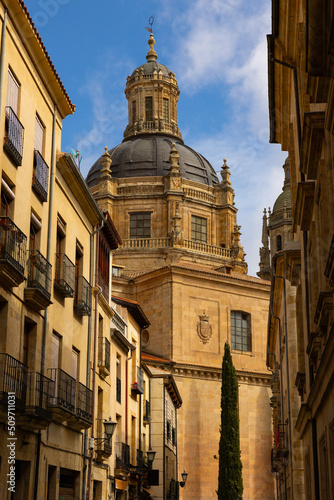 Scenic view of huge baroque dome of La Clerecia against blue spring sky dominating narrow street with residential townhouses in historic district of Salamanca, Spain