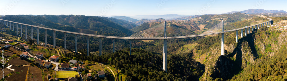 Picturesque panoramic aerial view of high modern suspension viaduct with highway crossing rocky gorge