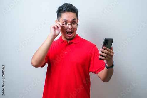 Asian young man looks surprised at the good news he received from his smartphone © Reza
