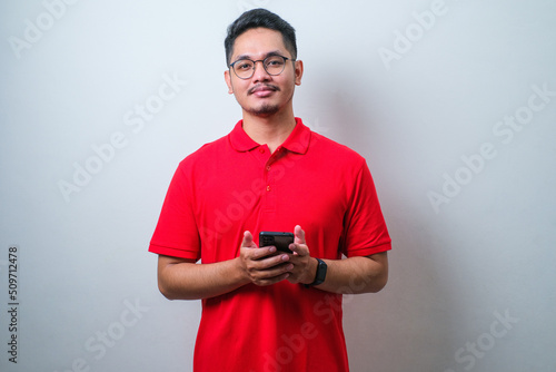 Portrait young Asian man in casual red shirt using smartphone trading or chatting