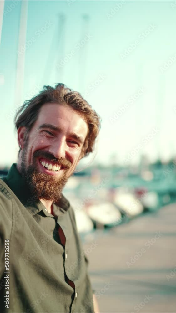 VERTICAL VIDEO: Closeup portrait of a smiling man with a beard chatting on the embankment, on a yacht background. Frontal close-up of happy young male hipster using mobile phone VERTICAL VIDEO: Closeup portrait of a smiling man with a beard chatting on the embankment, on a yacht background. Frontal close-up of happy young male hipster using mobile phone