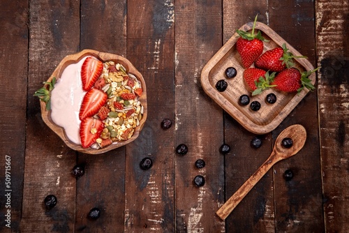 Yogurt and strawberry granola in wooden bowl.Decorated with blueberries on wooden background.Top view with copy space.