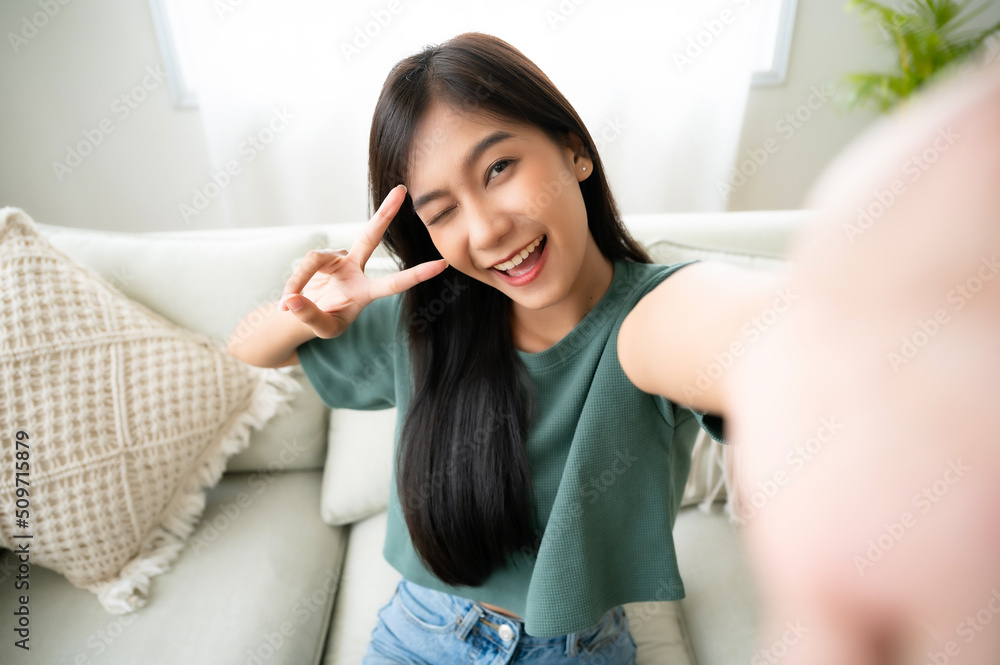 Pretty young asian female with big smile sitting at living room. She having fun taking light cheerful selfie on blurred background Pretty young asian female with big smile sitting at living room. She having fun taking light cheerful selfie on blurred background