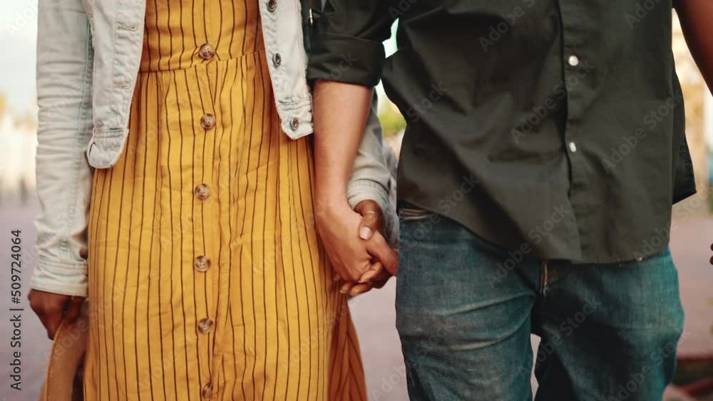 Closeup, man and woman walk holding hands. Close-up of the hands of a young interracial couple Closeup, man and woman walk holding hands. Close-up of the hands of a young interracial couple