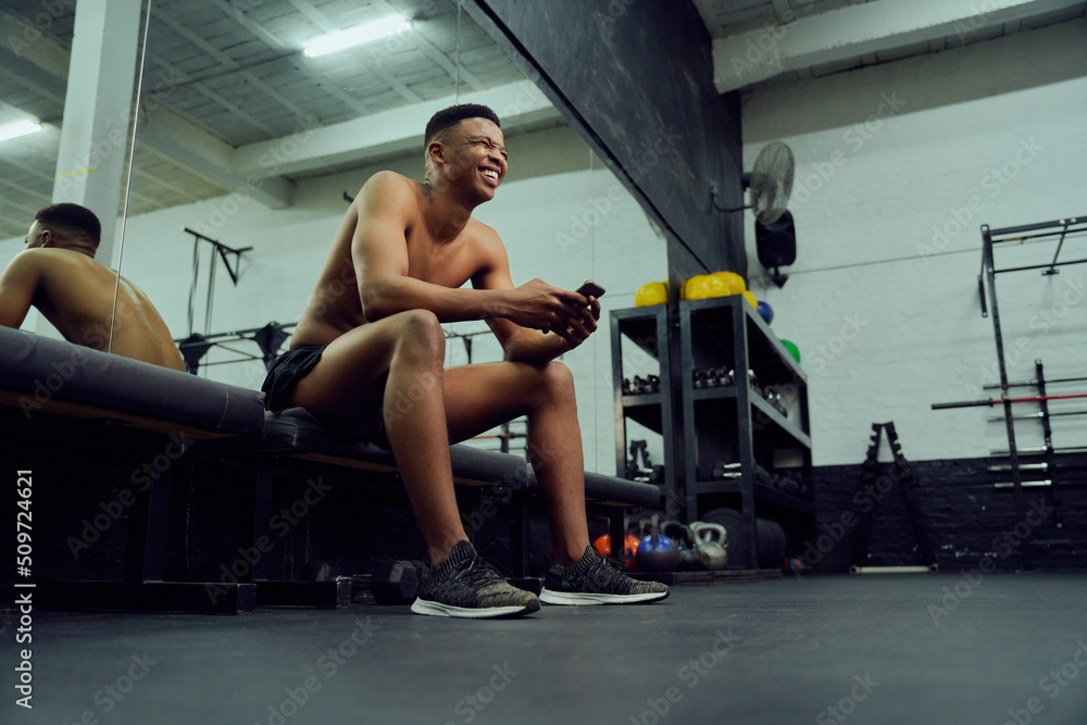 Young African American male looking at his phone to reply to an online message. Happy, mixed race male smiling at his phone while sitting down in the gym. High quality photo 